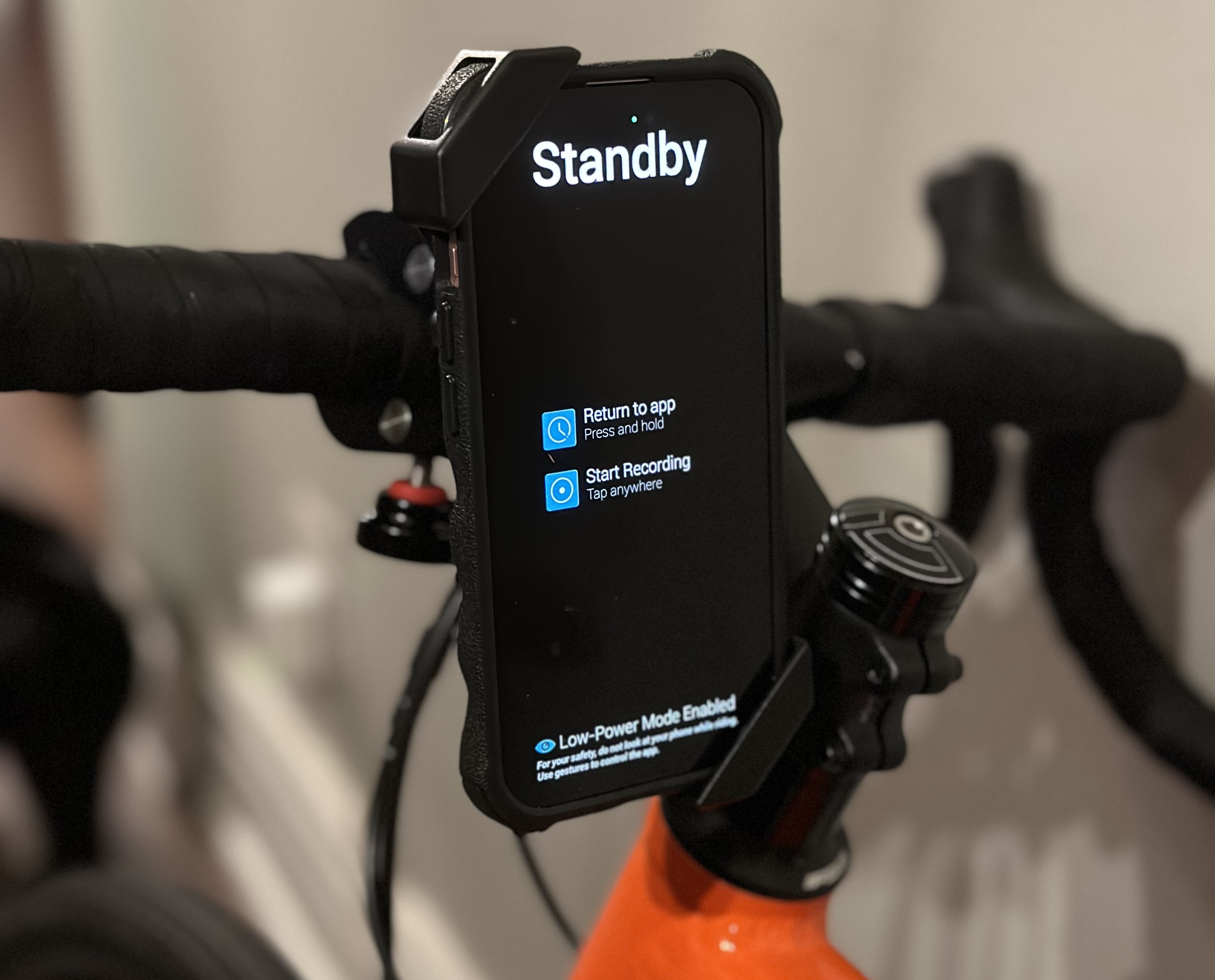 A smartphone running the dashcam.bike app, secured in the mount on road-bike handlebars